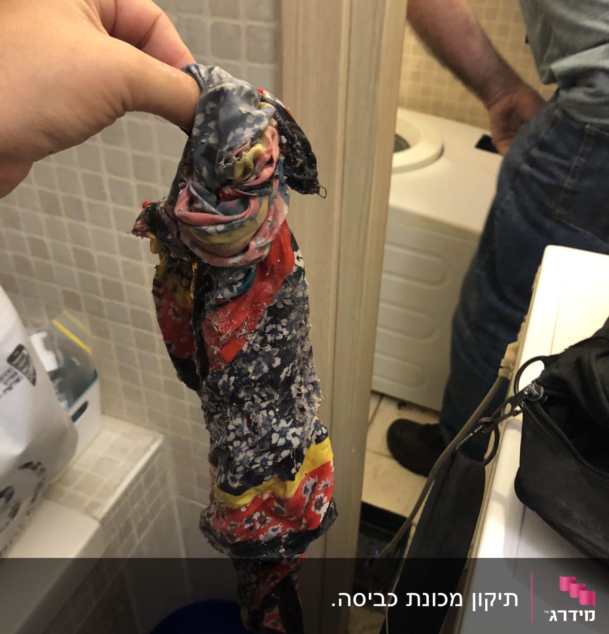 יד מחזיקה חפץ צבעוני ליד מכונת כביסה